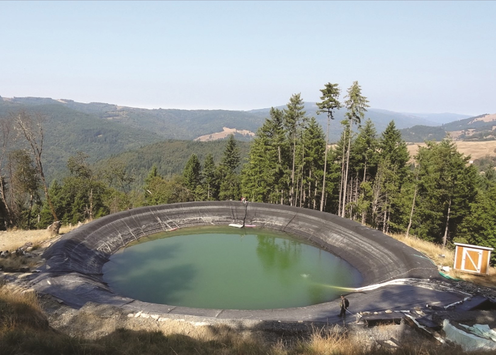 photograph of a circular lined pond, full of water, on a forested slope